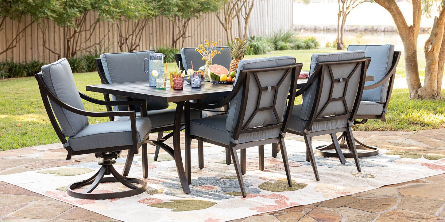 Outdoor patio furniture with a dining table, chairs, over a rug and a table set in the backyard