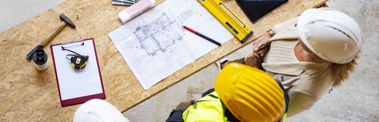 Contractor and client wearing hard hats looking at blueprints