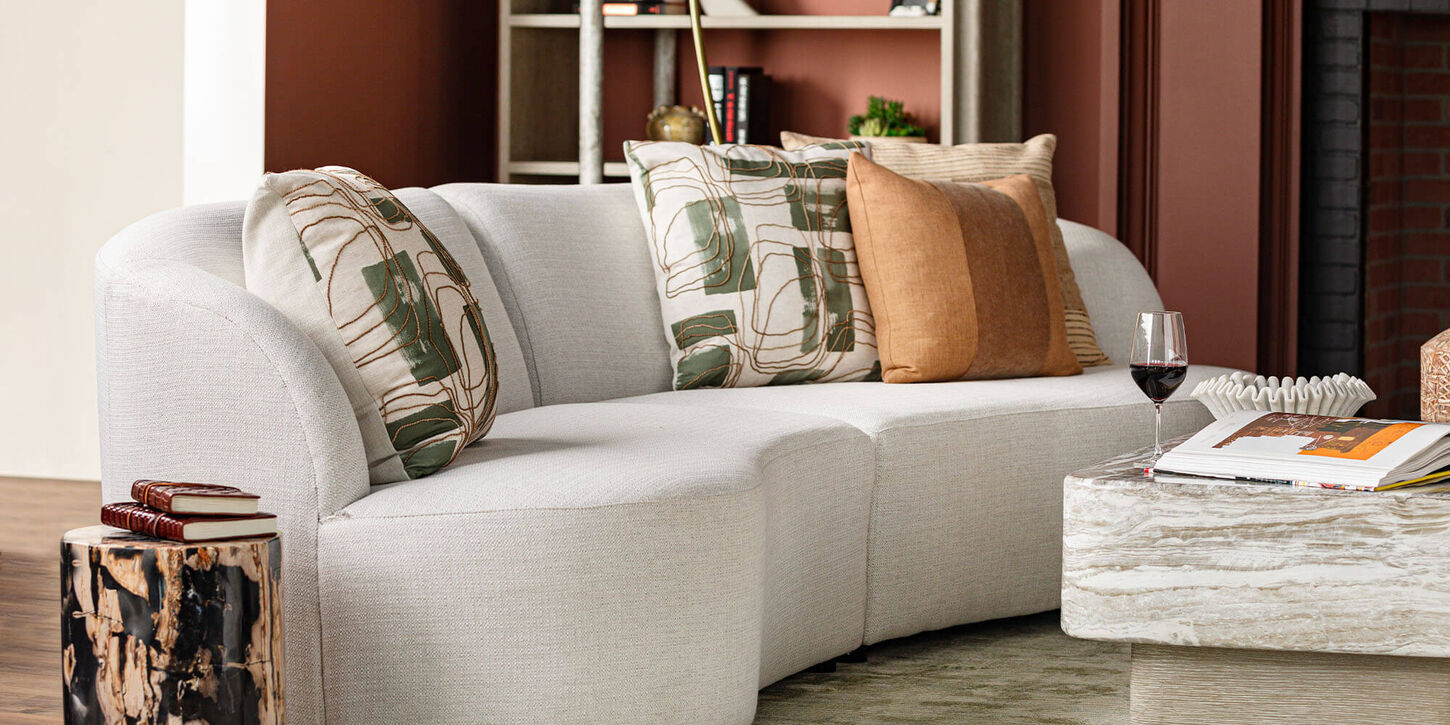Living room displaying a curved sofa, stone coffee and end table, earthy throw pillows and a bookshelf with decor