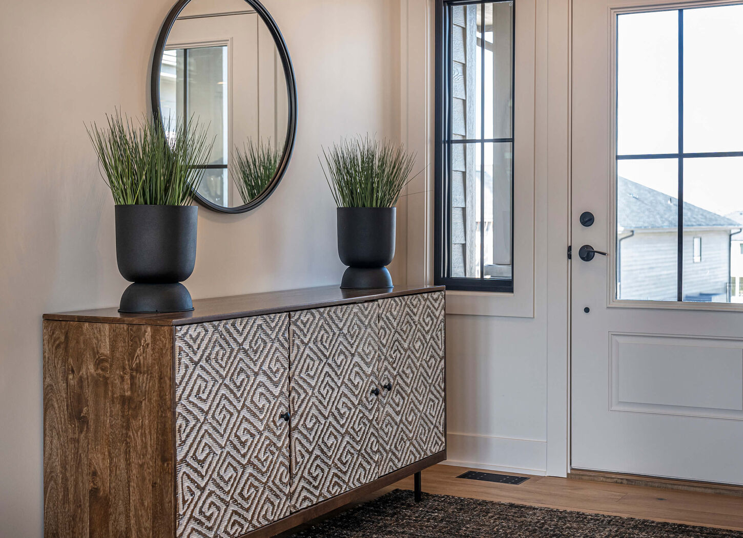 An entry way table with two plants and a circle mirror.