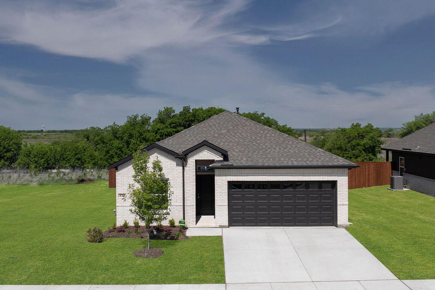 A bigger picture of a model home overview. Designed with a living area and an entry way space that includes a couch, chairs, entry table, and plants. Entire area gives an earthy tone.