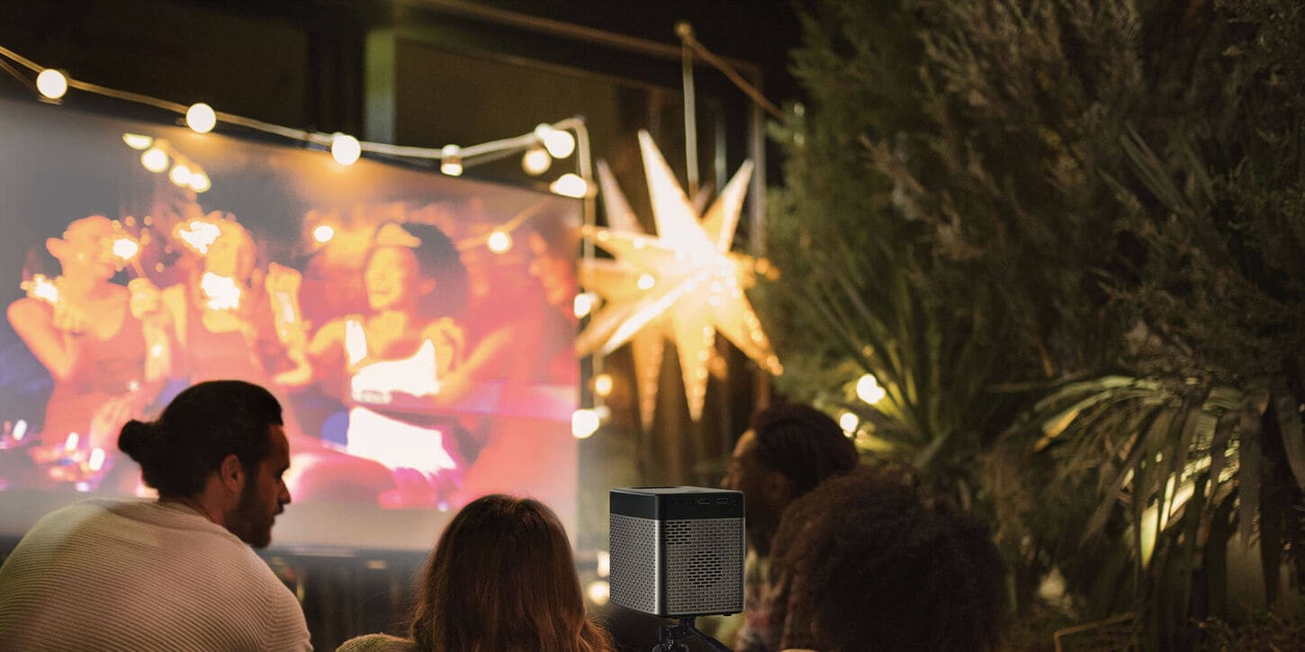 Couple and friends sitting outside watching a projector with lights hanging in the trees