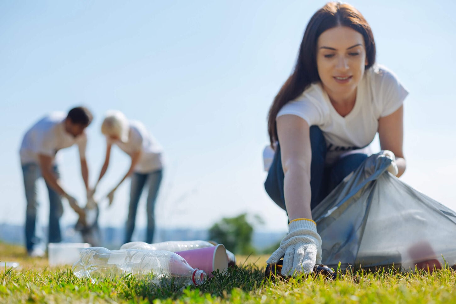 A woman outside picking up trash along with two others in the background also picking up trash.