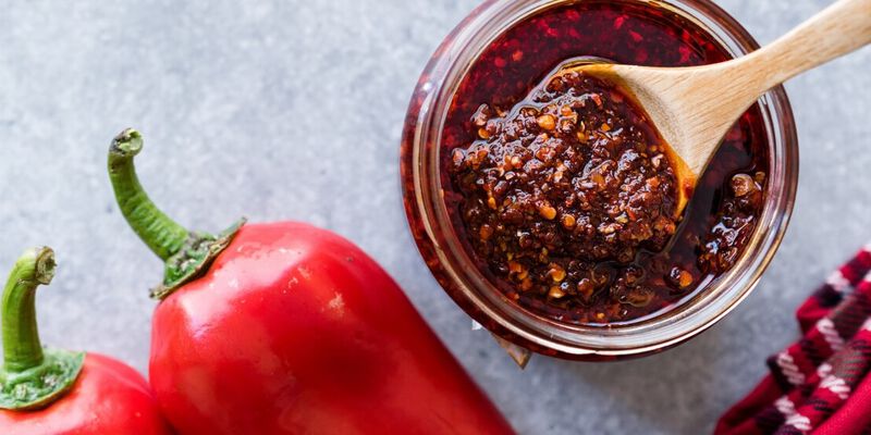 Cup of homemade hot sauce next to red chili peppers.