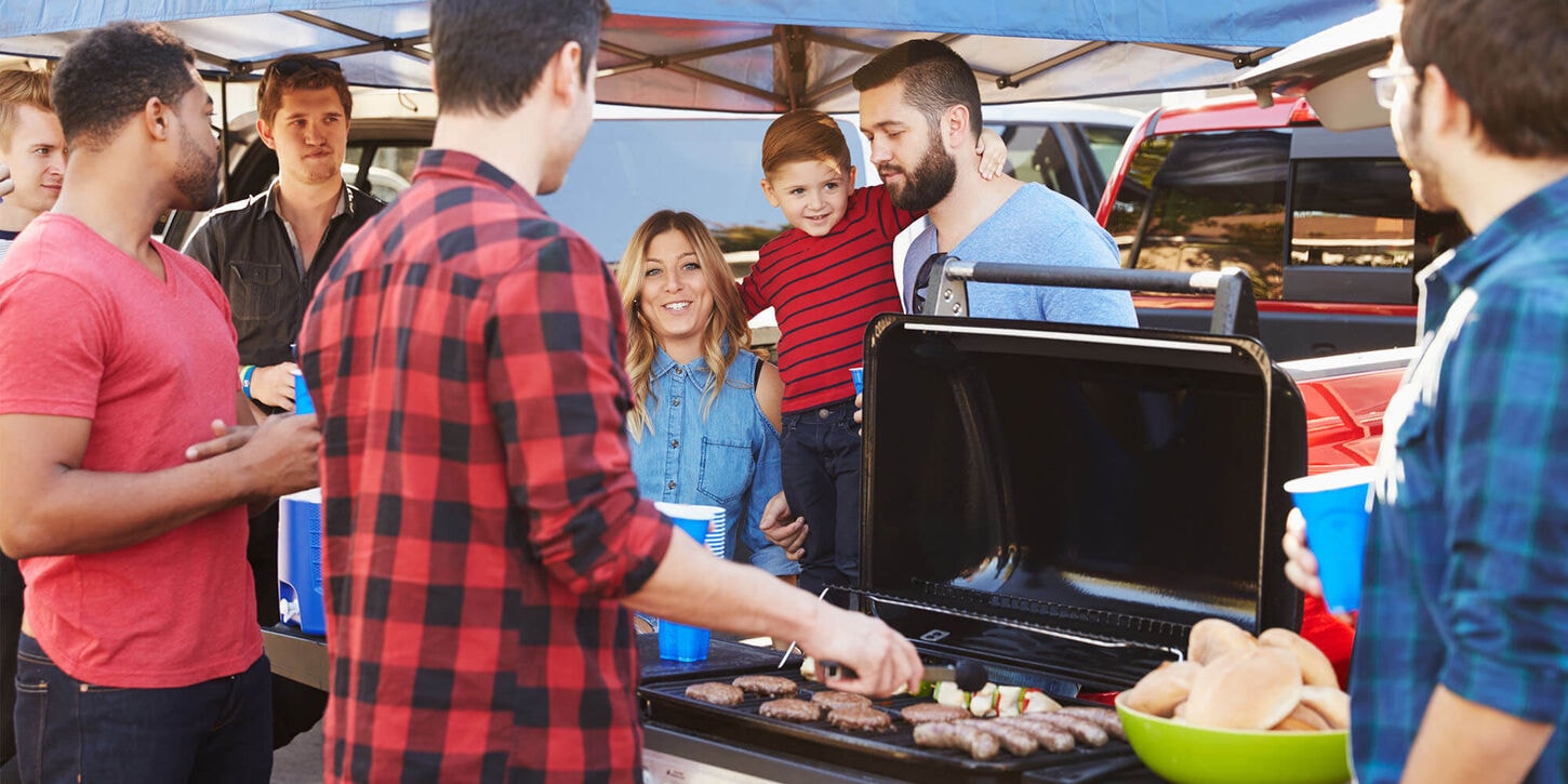 Big group of people tailgating at a football game and grilling hotdogs on a grill