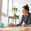 A woman works intently on her laptop at a bright, inviting table.
