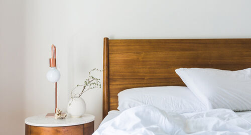 Bed with natural wood headboard with round modern nightstand along the side