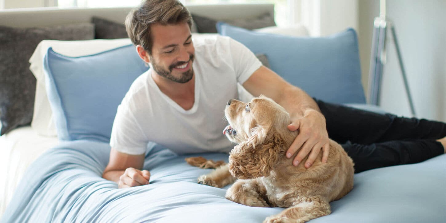 Man on his bed petting his dog with a blue comforter and pillows