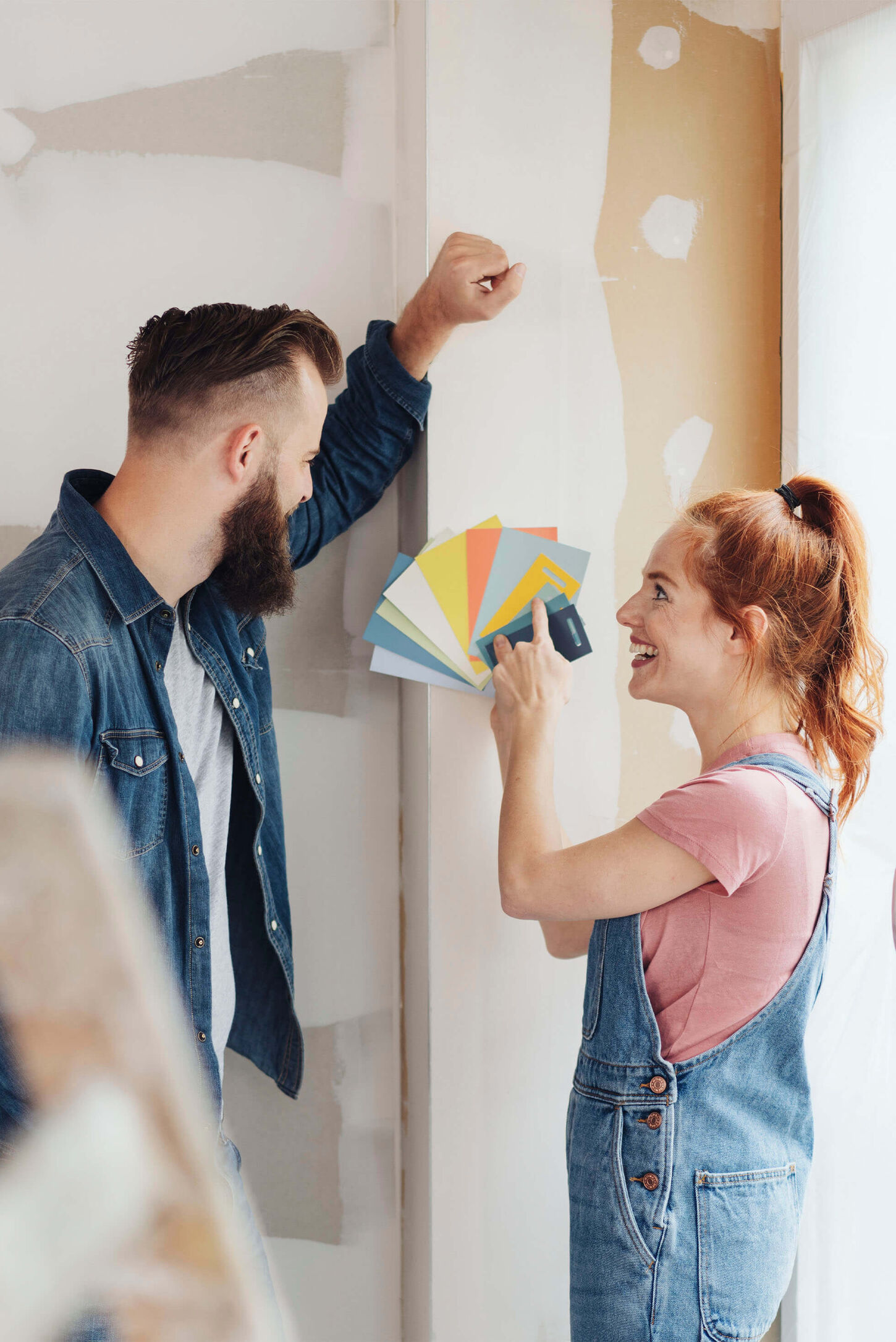 Husband and wife holding up paint colors to a wall