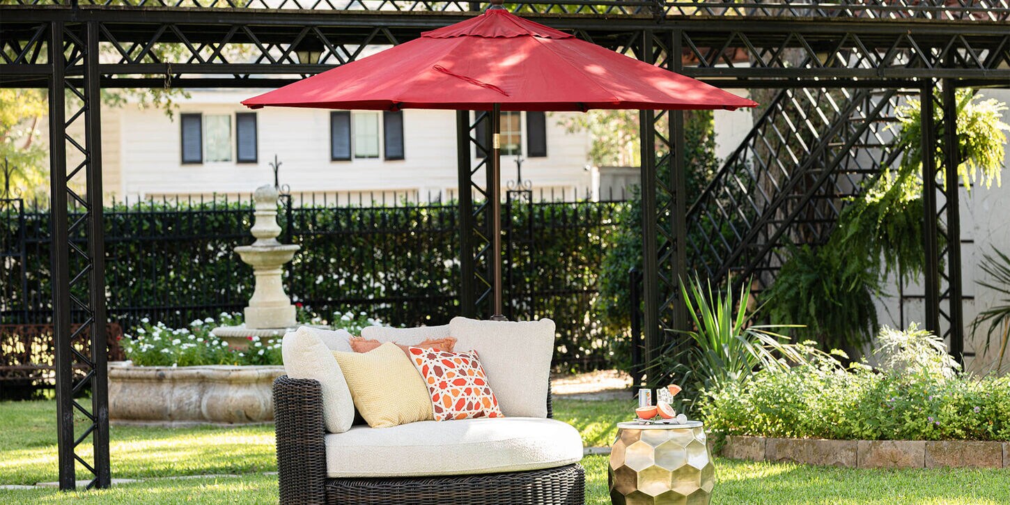 Outdoor patio furniture with a large round chair, pillows, and a big umbrella hanging over