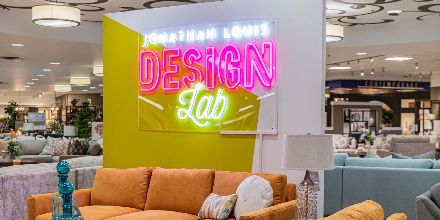 Jonathan Louis Design Lab neon sign inside of NFM with various couches around the area in orange, blue, and tan.