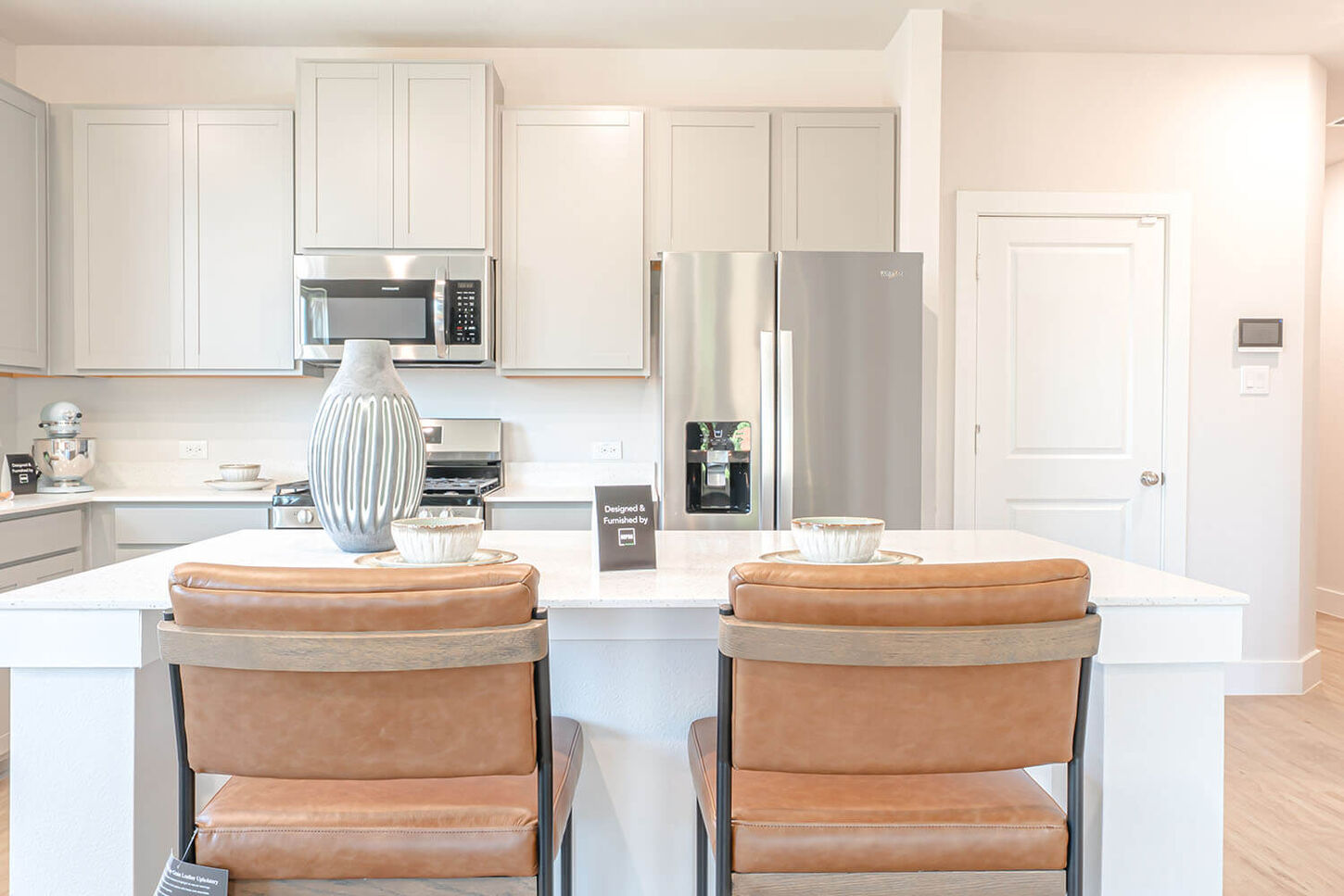 Bright kitchen with two bar stools, stainless steel appliances, and a door