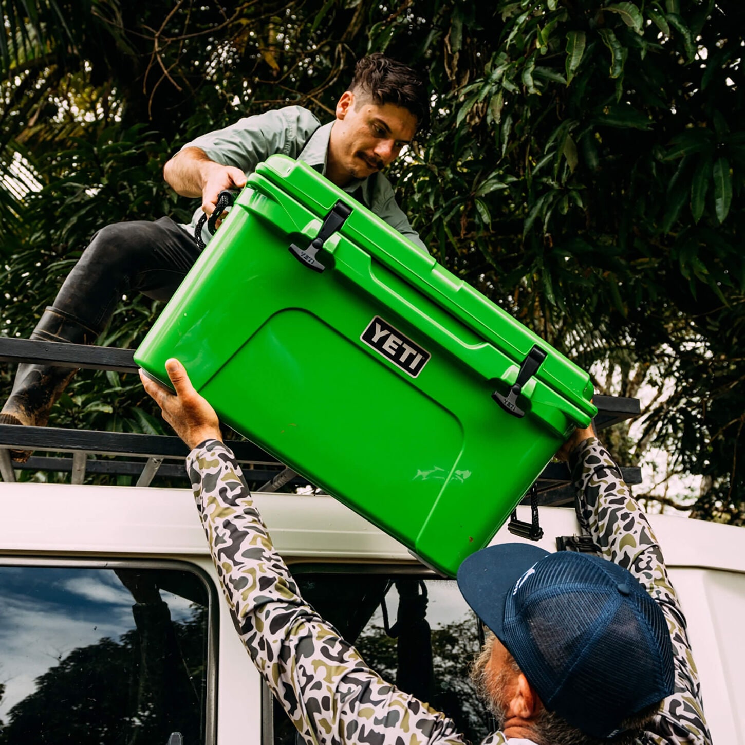 A yeti cooler being taken down from the roof of a car by two guys. 