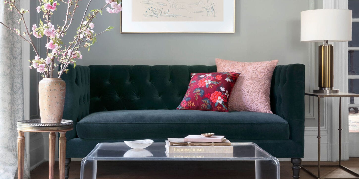 Living room with a blue sofa, bright throw pillows, lamp, coffee table and a dainty vase full of flowers