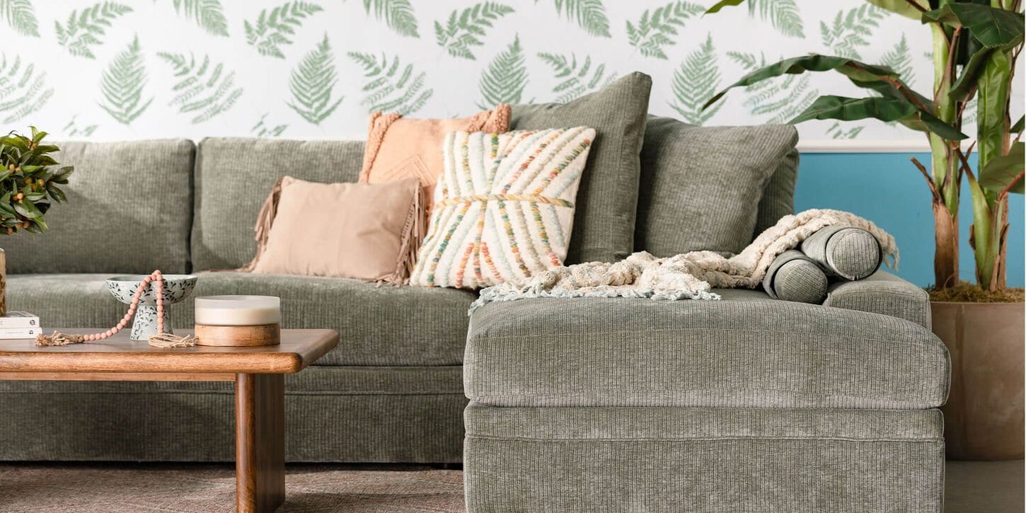 Section sofa with coffee table and lots of pillows and plants and a leafy wallpaper on the walls