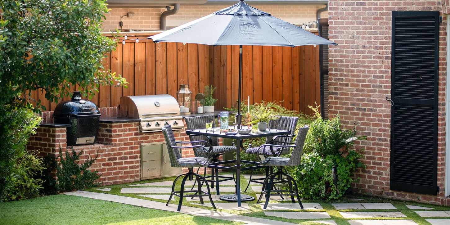 Outdoor patio furniture with dining table, next to grill with an umbrella in the backyard