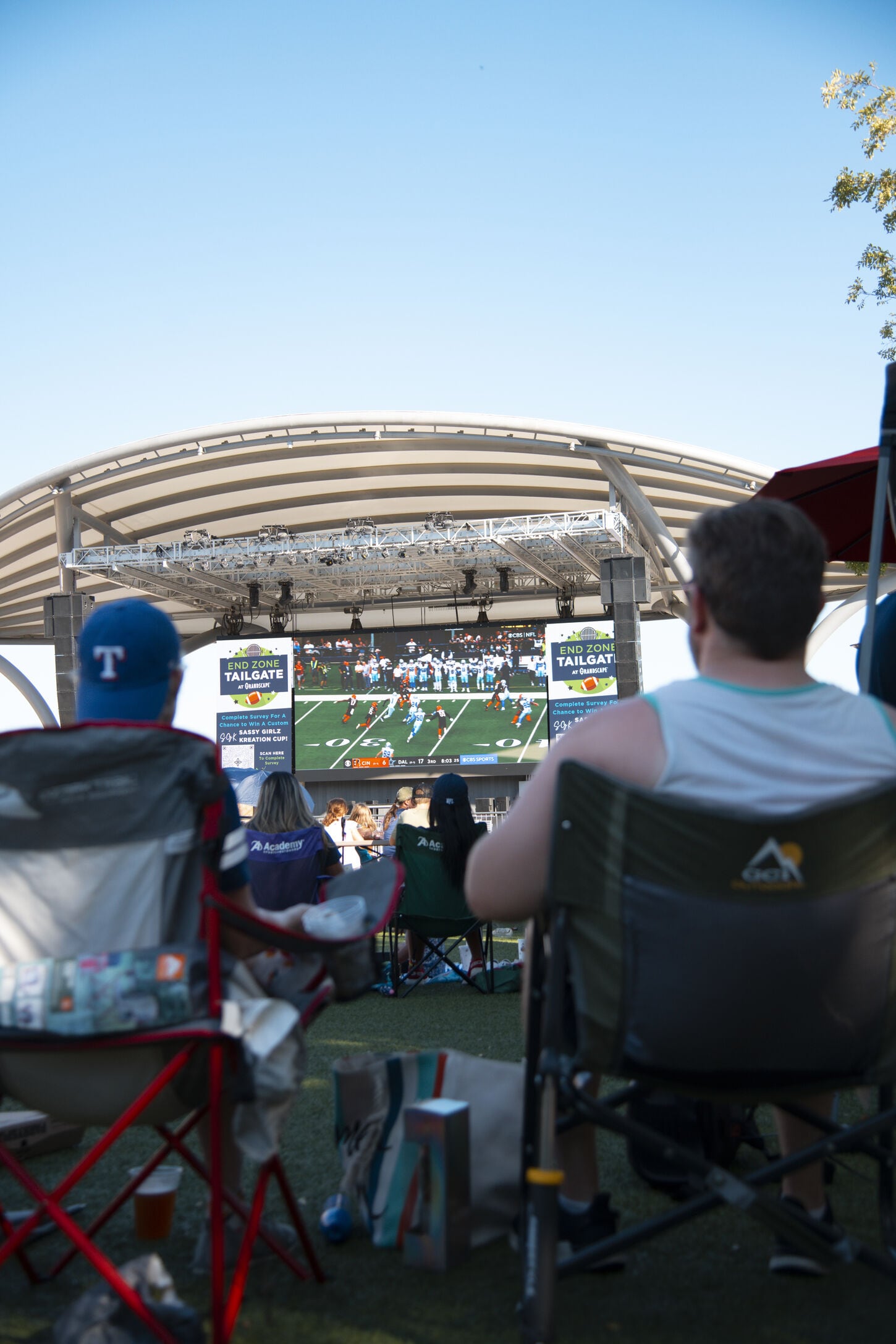 Two men sitting at tailgating watching the game on a big screen 