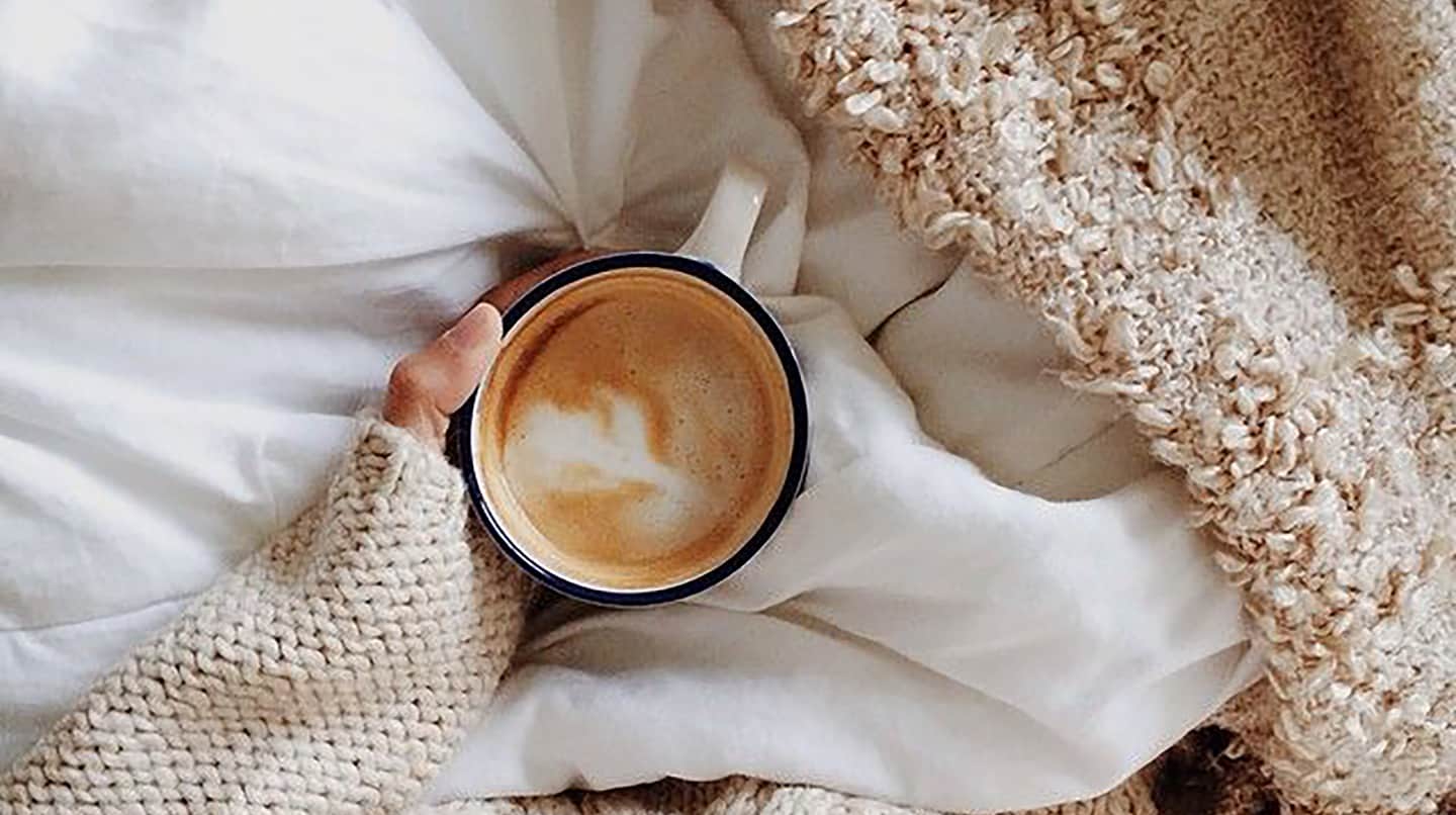 A latte being held by someone laying in cozy bedding