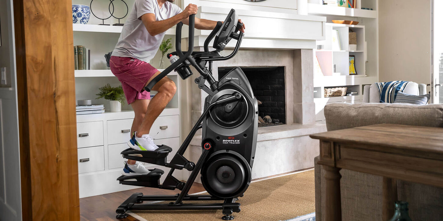 Someone in their home on an elliptical machine working out.