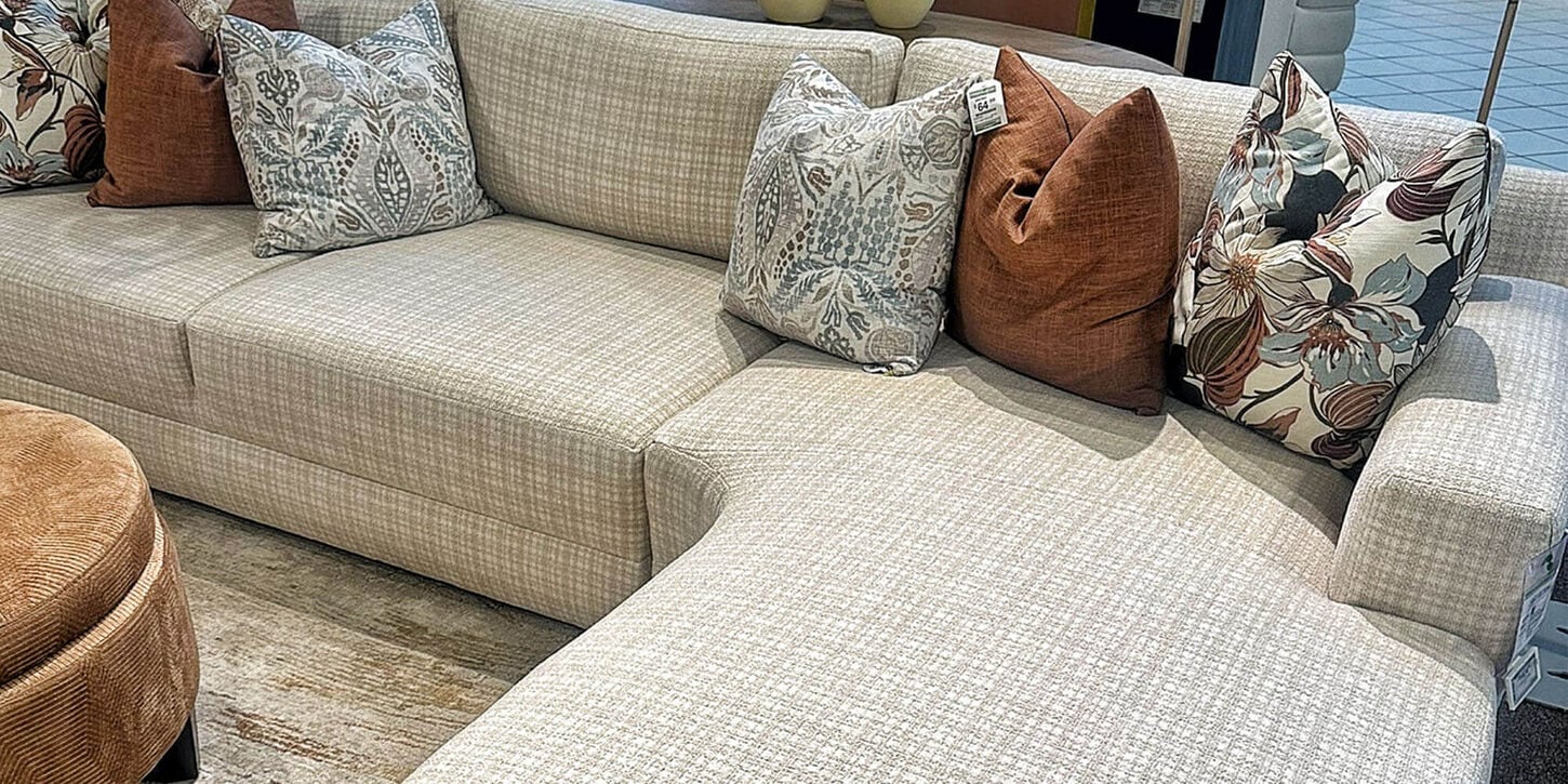 Custom couch inside of NFM in a tan color with various pillows, a rug and side of a coffee table.