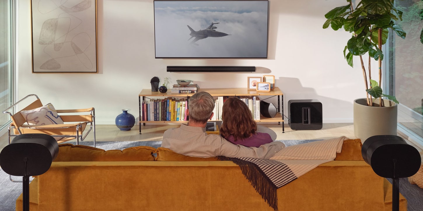 sonos speakers in living room behind a couch with a couple sitting and watching tv