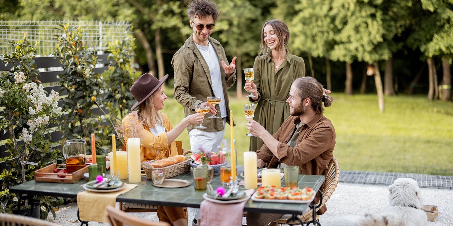Friends outside sitting at a dining table cheersing each other in the backyard
