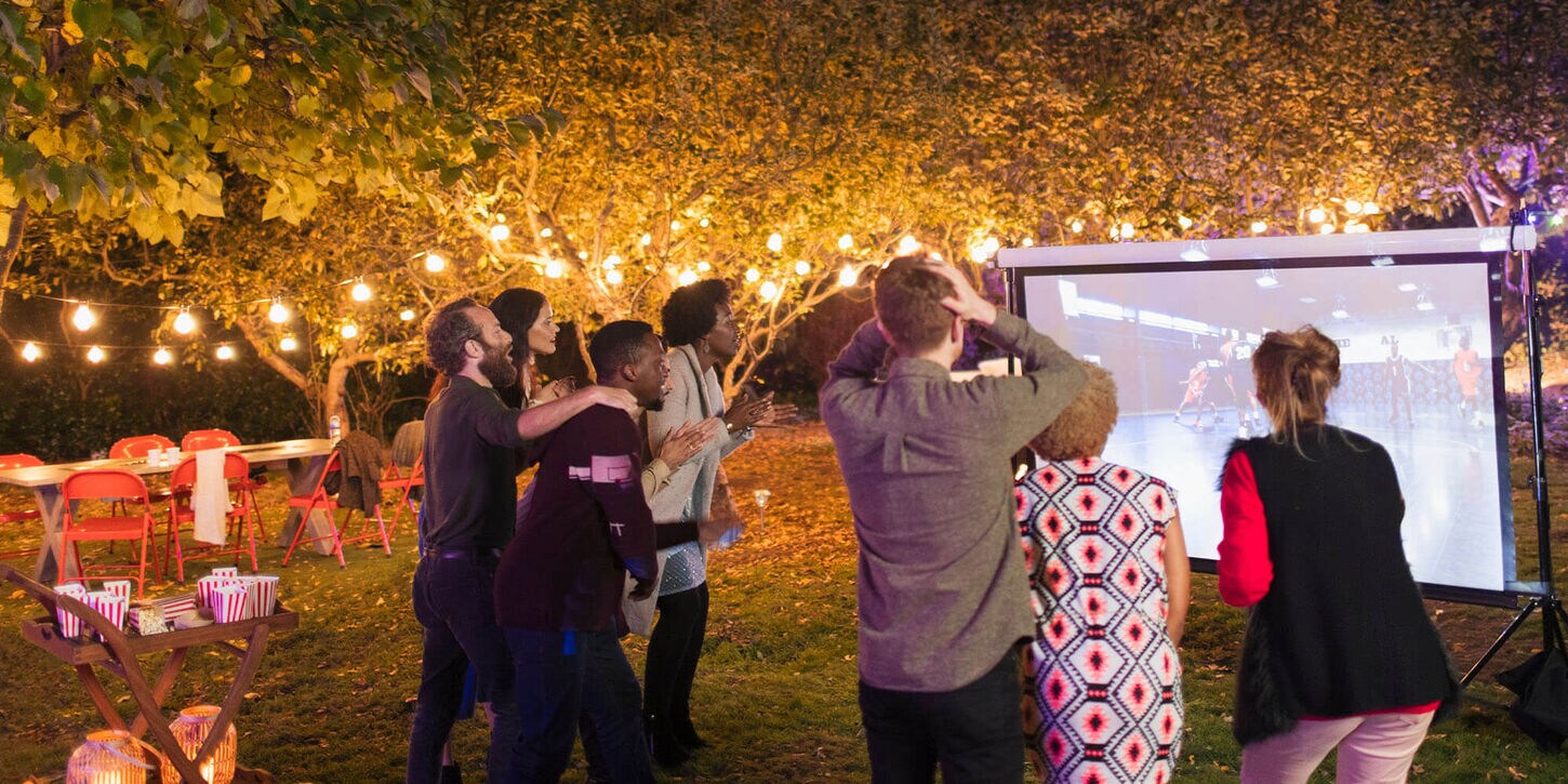 Family sitting outside in the backyard grilling and watching a football game on the tv