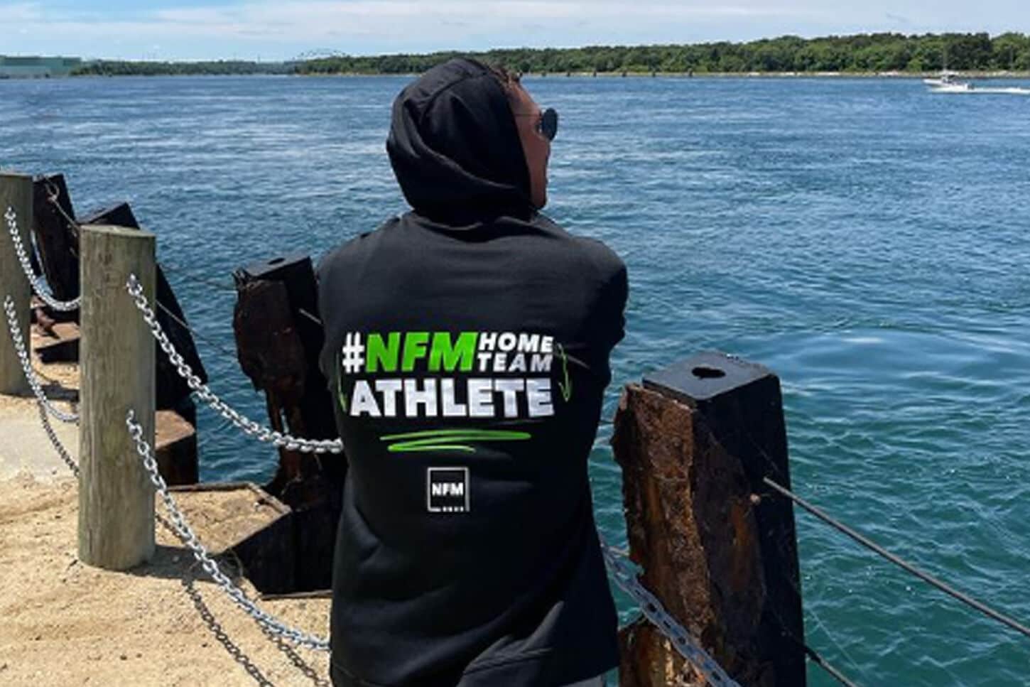An NIL athlete posing in their sweatshirt with their back towards the camera looking at a lake,
