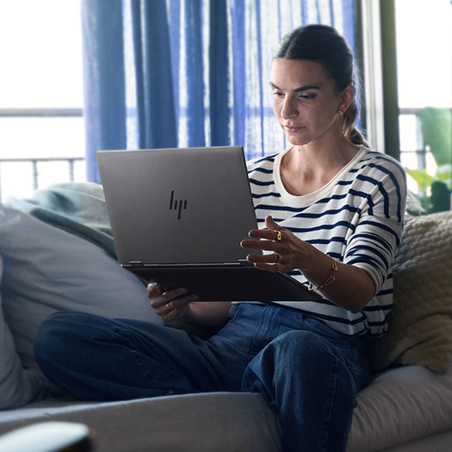 Woman sitting on couch, holding and looking at HP laptop