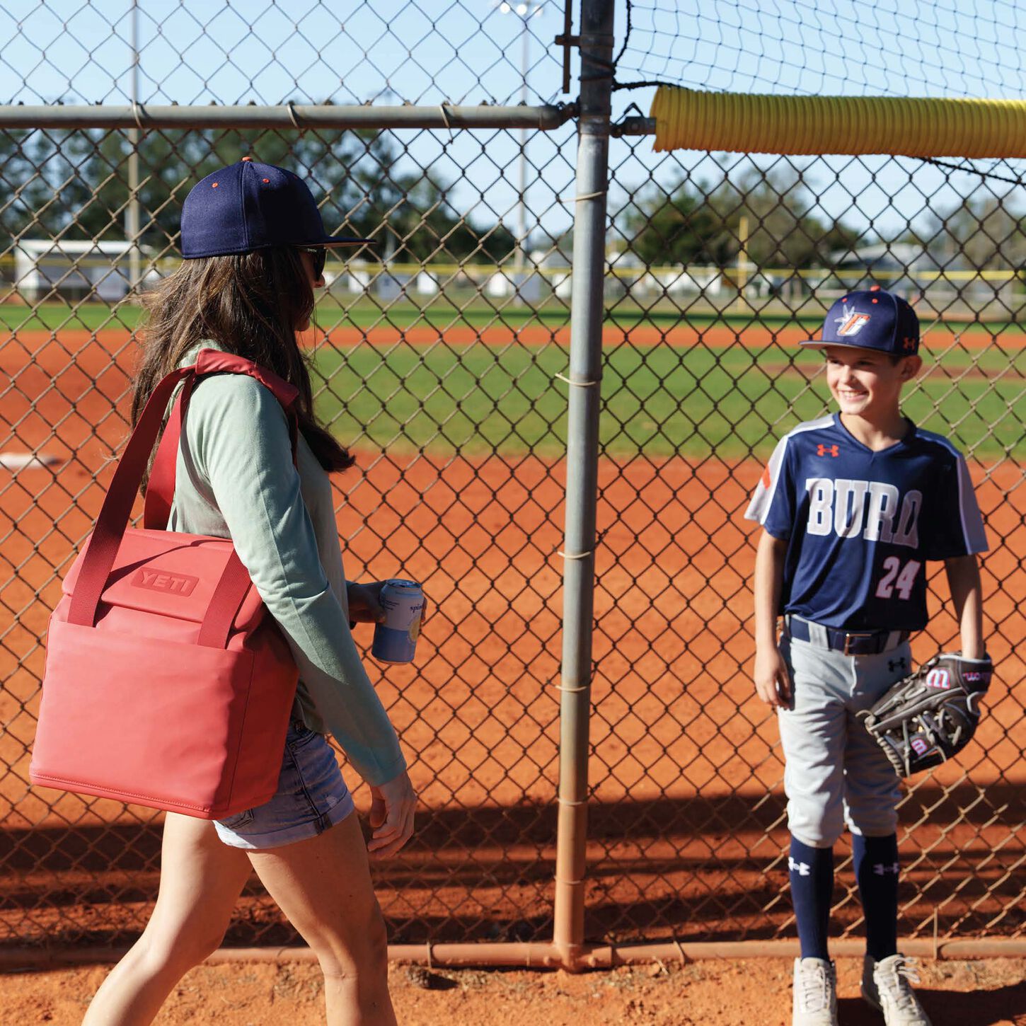 women carrying a pink yeti soft cooler looking at a child in a baseball uniform at a baseball feild