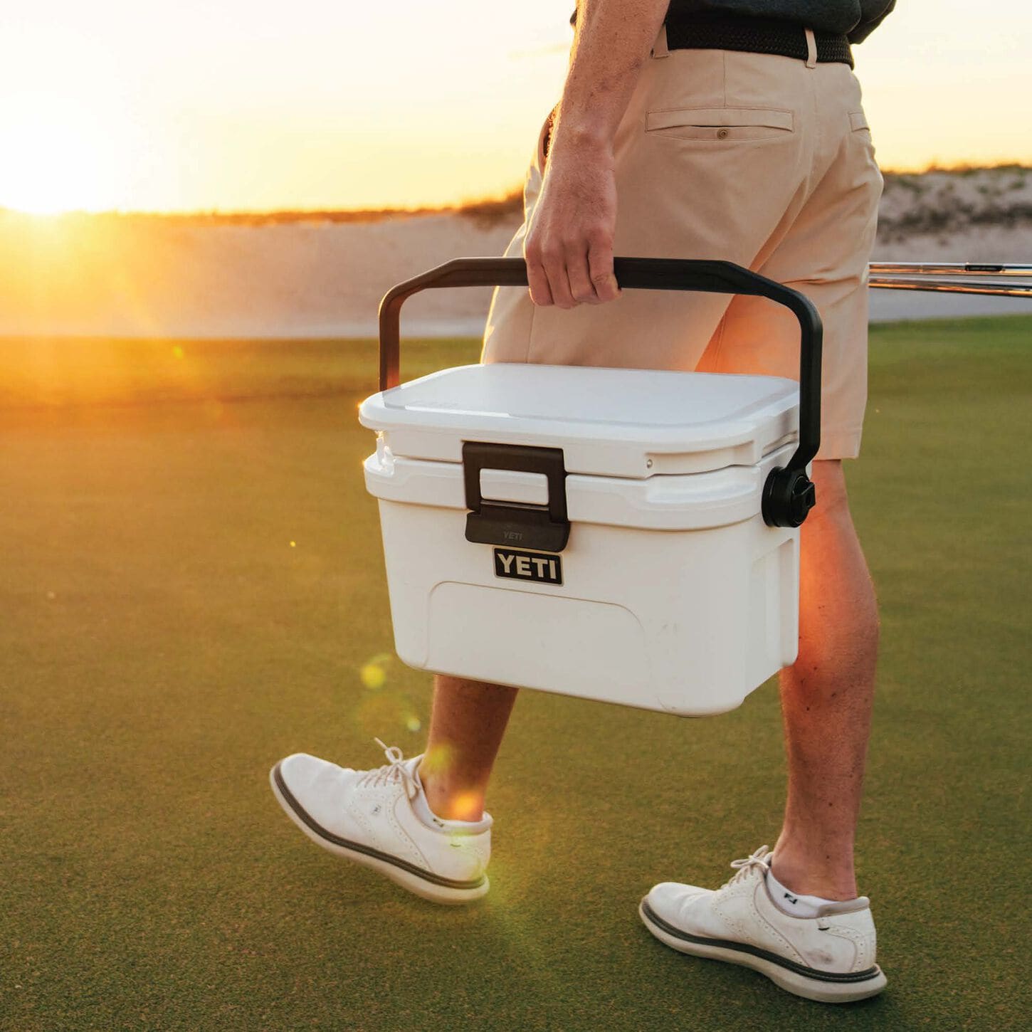 person carrying a white yeti cooler with the sun setting in the background