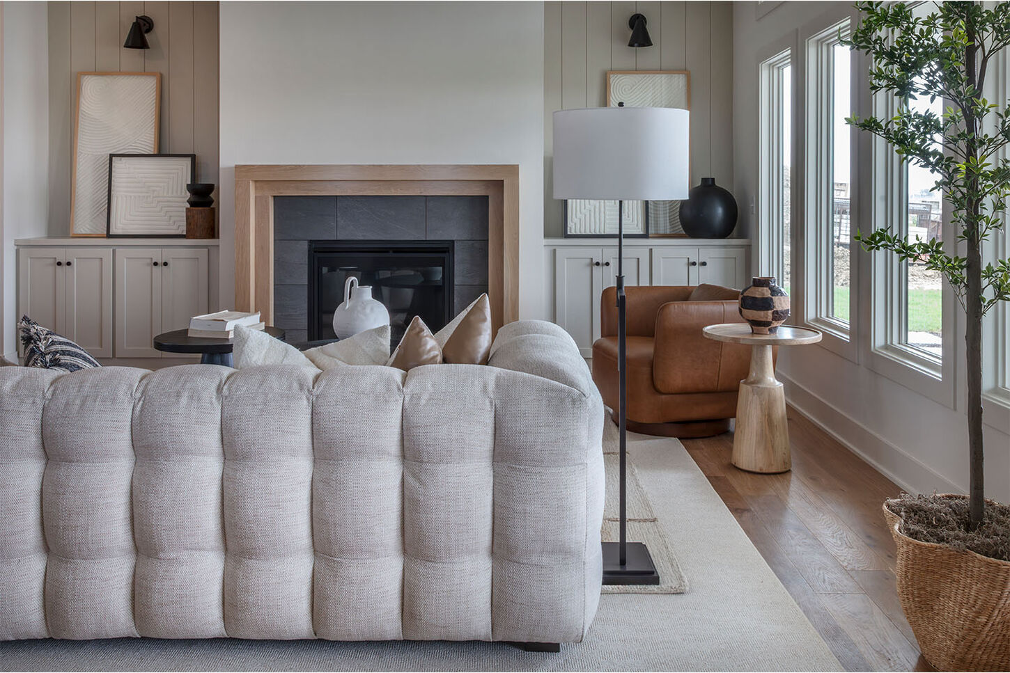 A bigger picture of a model home overview. Designed with a living area and an entry way space that includes a couch, chairs, entry table, and plants. Entire area gives an earthy tone.