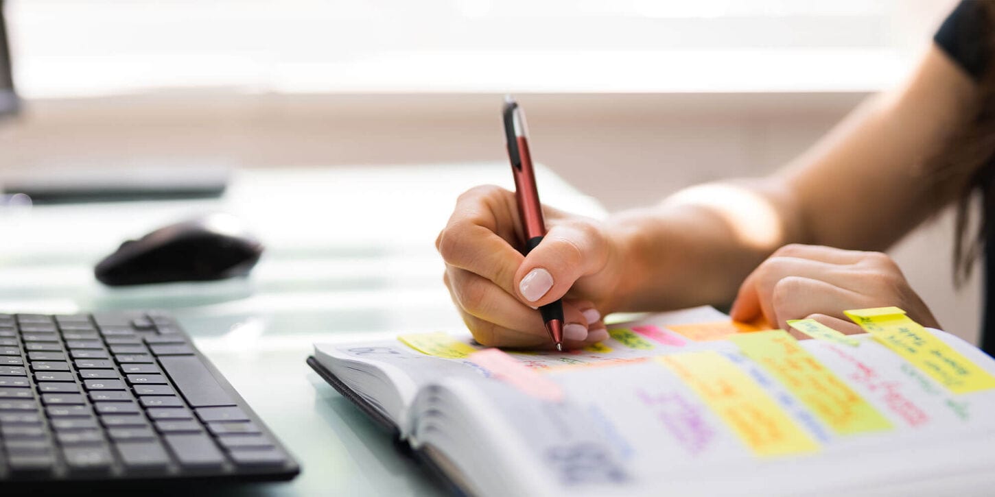 Woman planning a move and writing in a notebook on a desk near a keyboard and mouse