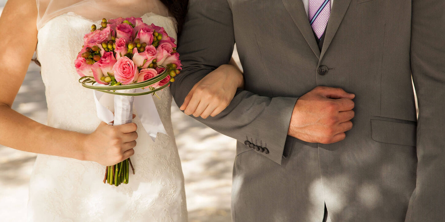 Man and woman on their wedding day and holding flowers while locking arms