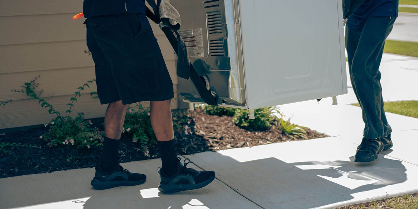 Two people moving a large appliance into a home
