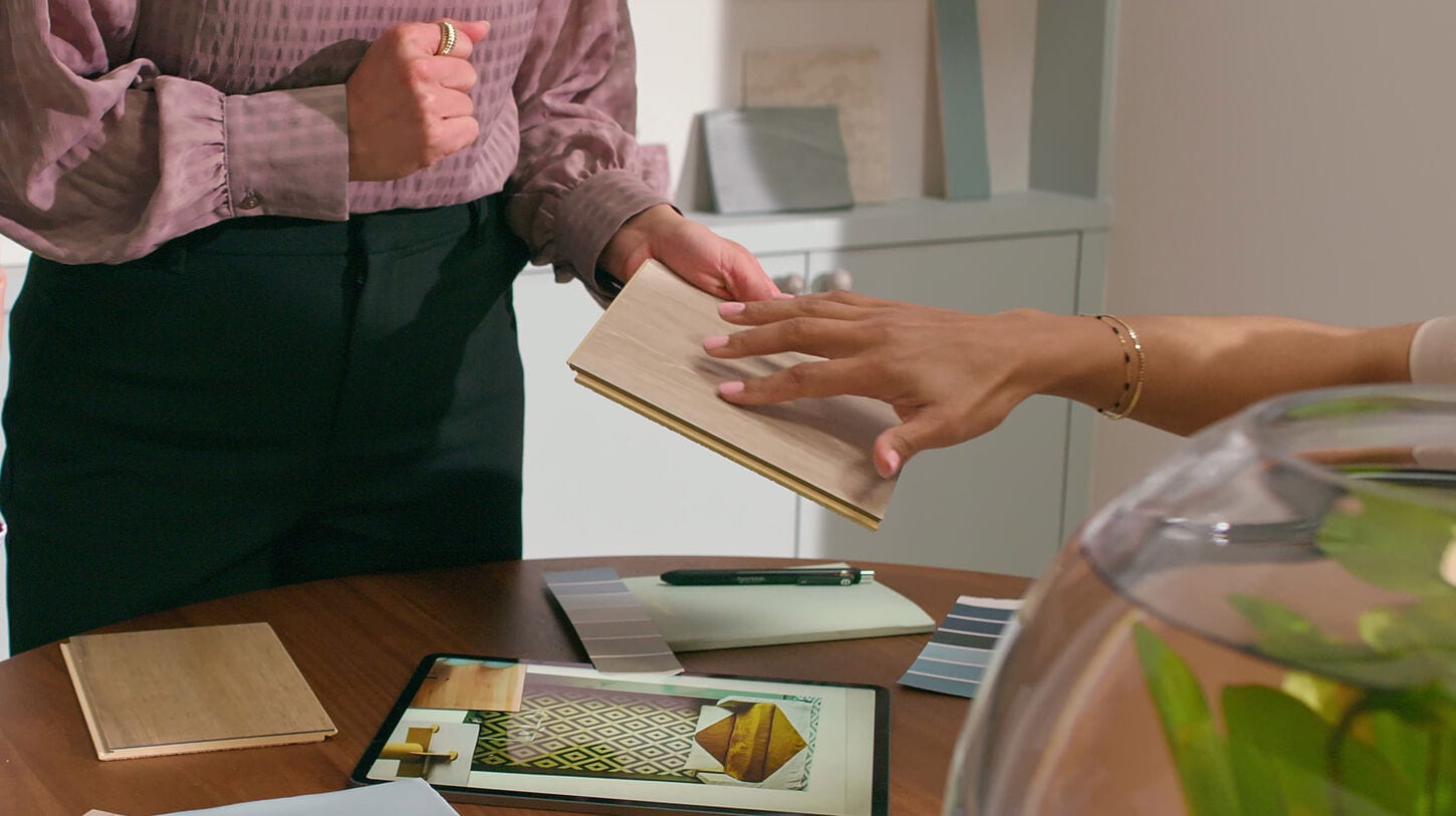 Two people selecting flooring samples at a table with color swatches, and a pen.