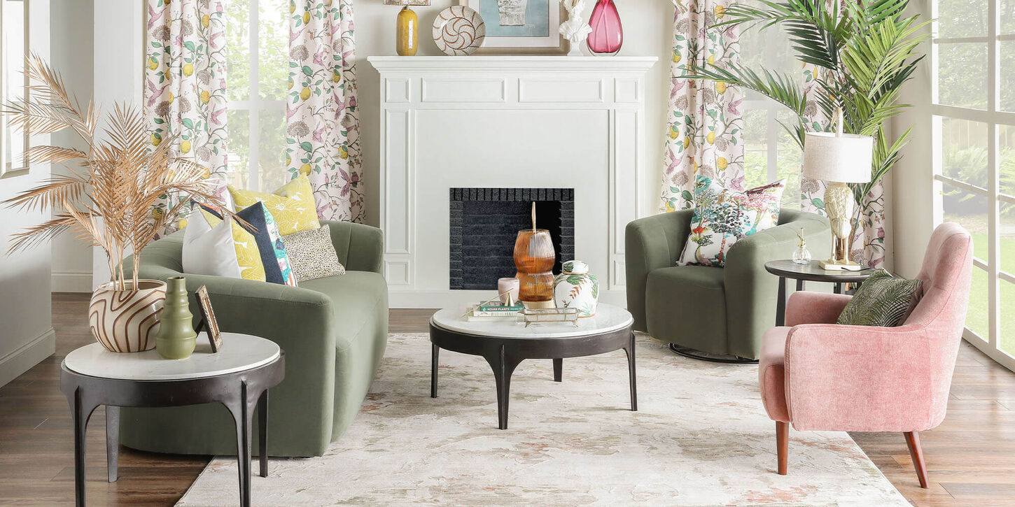 Bright living room with various colors including green and pink sofas and chairs, large rug, big windows and a fireplace.