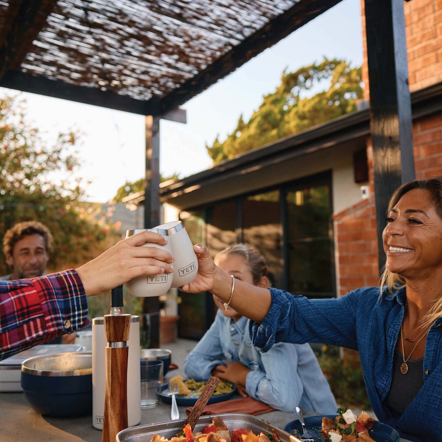 people sitting at a table in an outdoor scene toasting with two white yeti glasses