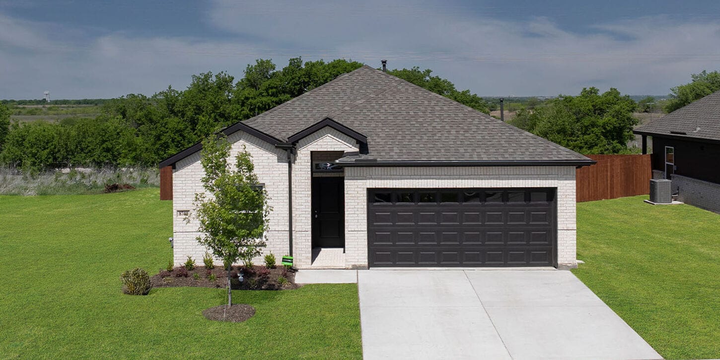 First Texas Home model house with white brick, a black garage, and greenery and trees around the home