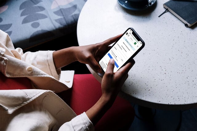 Person holding mobile phone at coffee shop logging onto nfm.com website