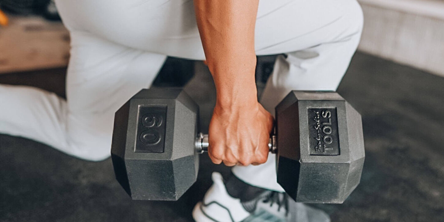 Someone holding a 50-pound free weight in their home gym and lunging.