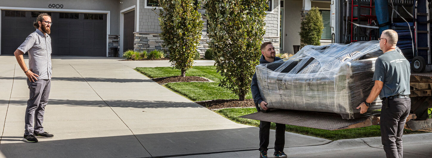 Two people carrying furniture from delivery truck into home