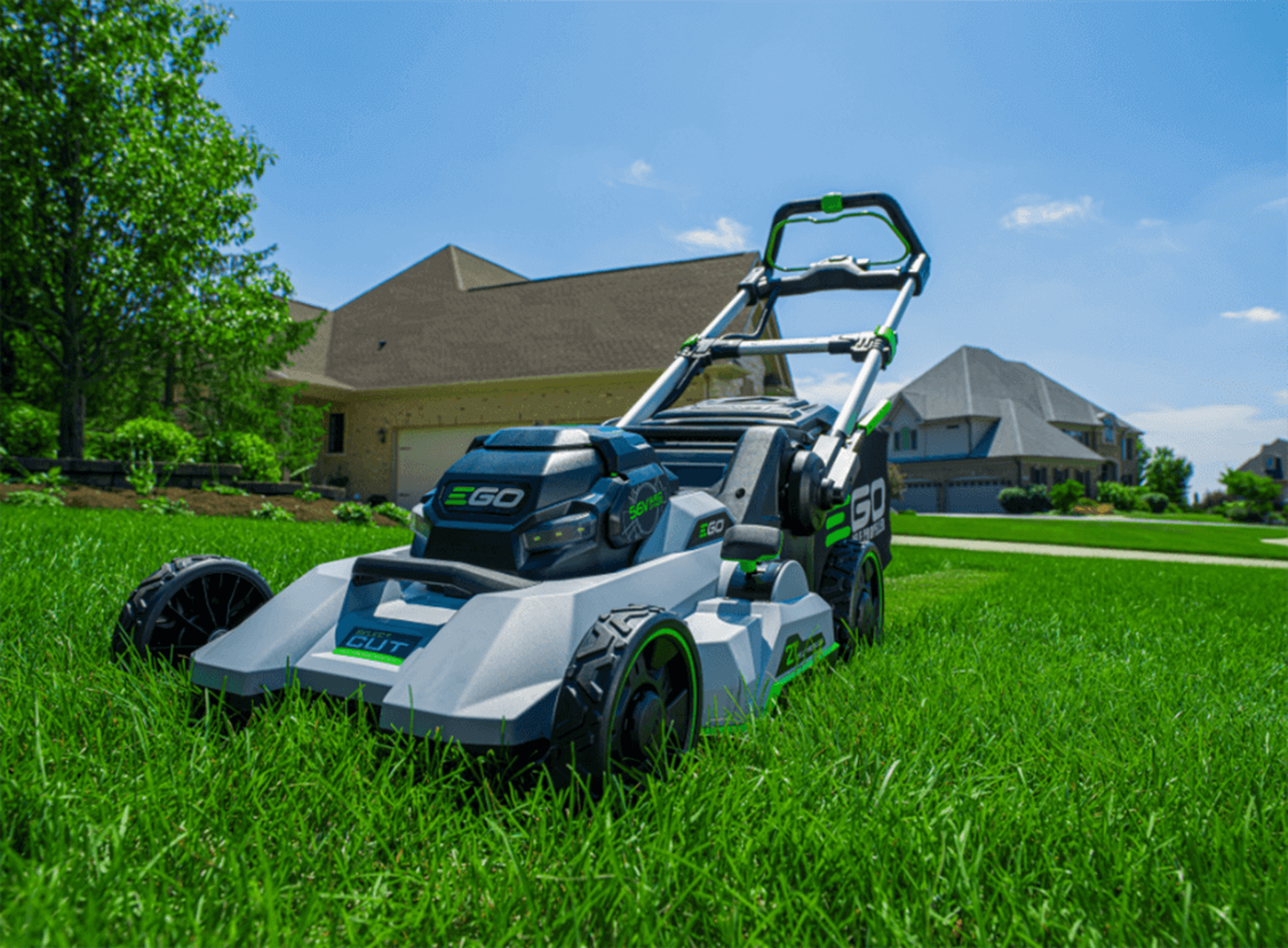 An eGO lawnmower in the lawn in the front of a house.