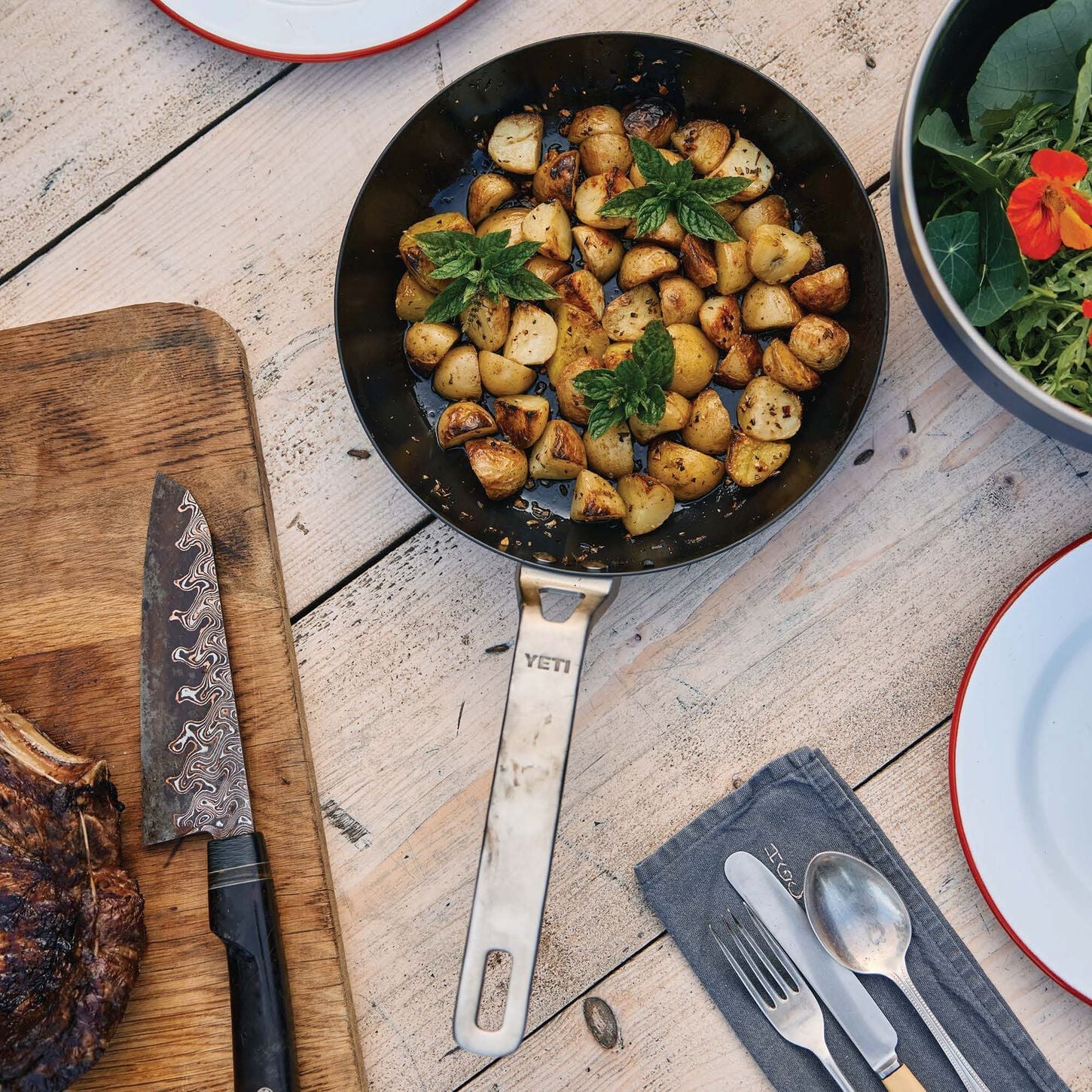 a frying pan on a table with a cutting board knife and silverware