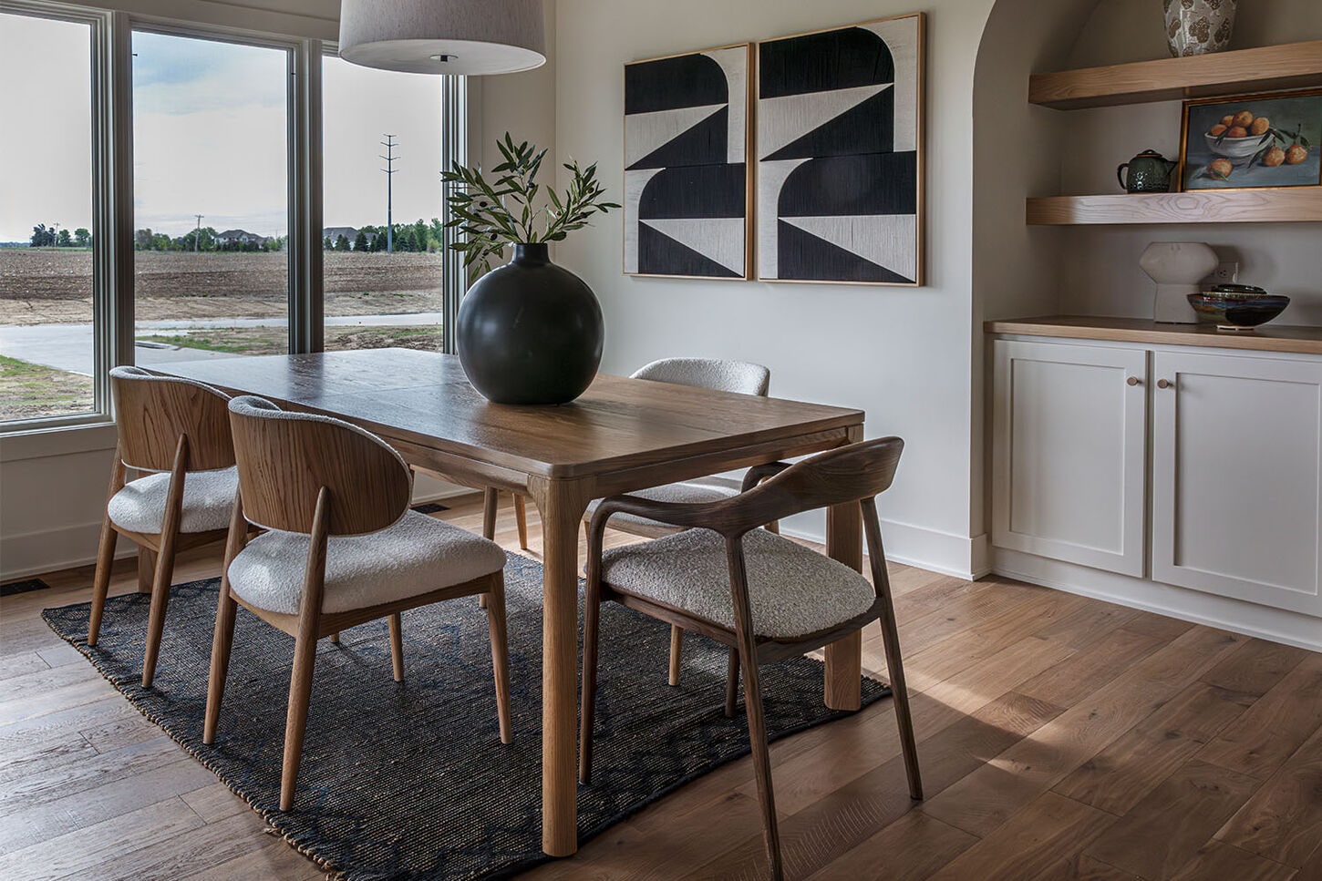 A dining room table with 6 chairs on a striped rug under a black chandelier. 