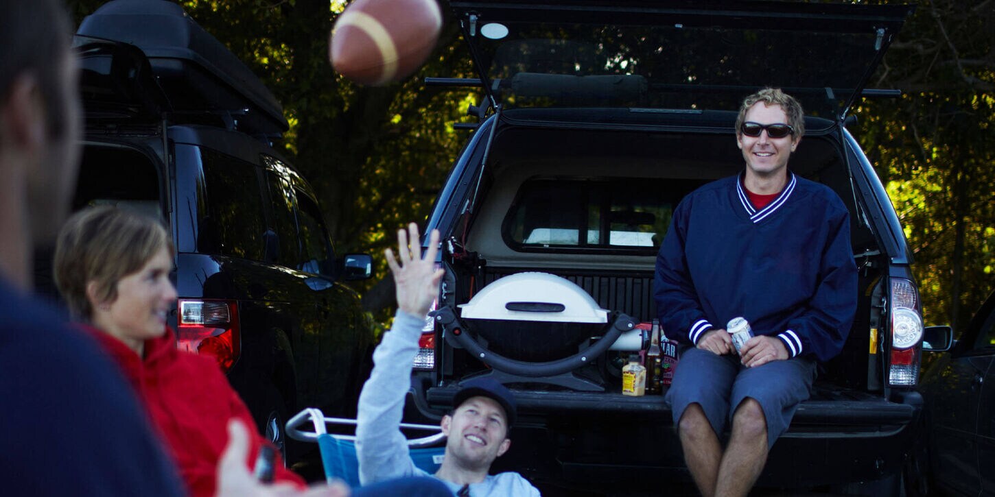 People tailgating, sitting in the back of their trucks and throwing a football