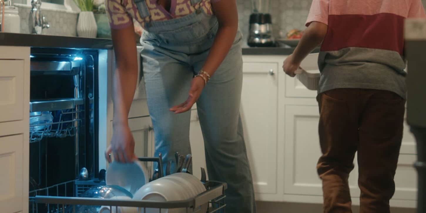 LG dishwasher open with a few people unloading it in the kitchen
