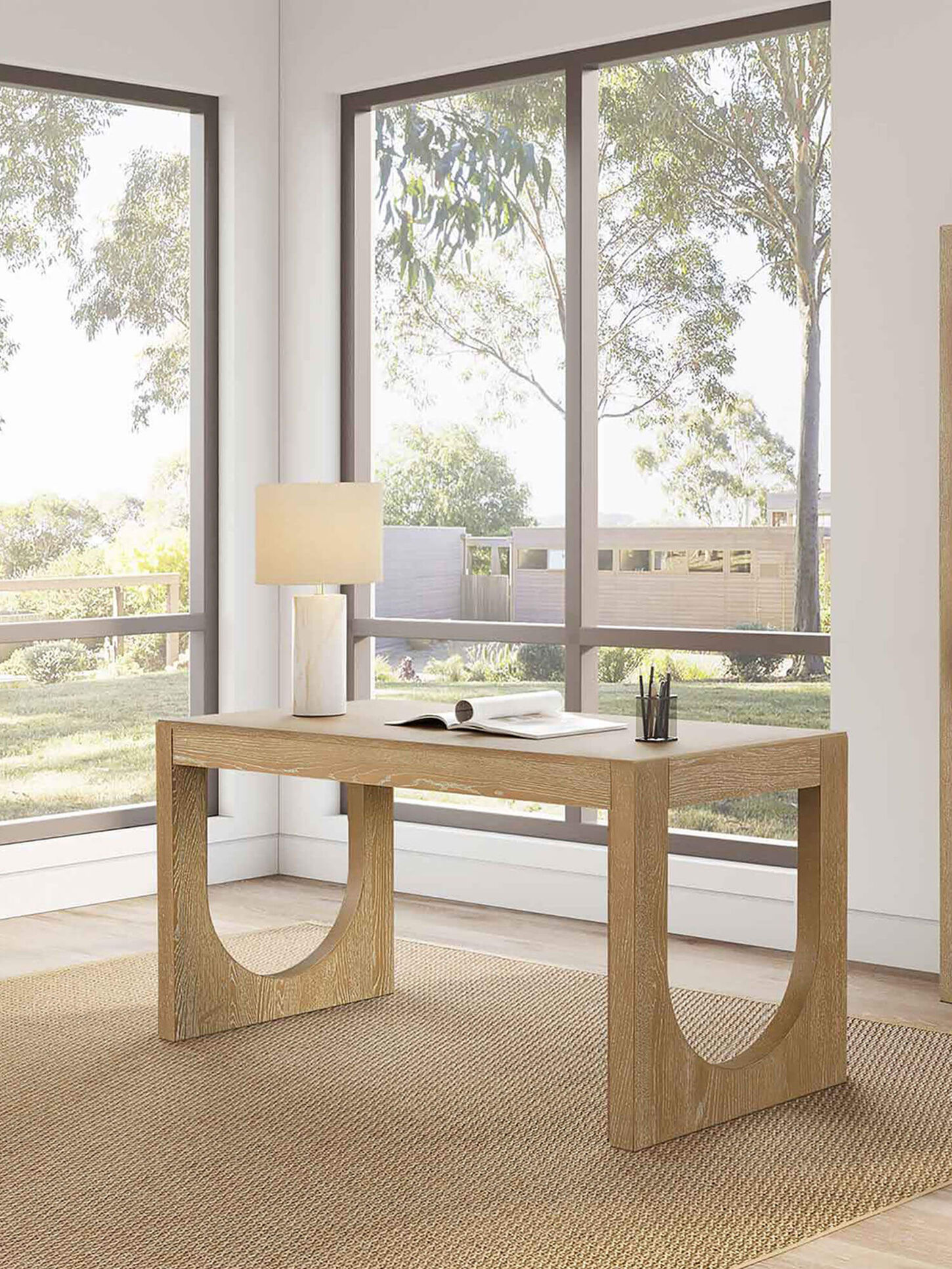 Light wood desk in a home office with big windows in the background.