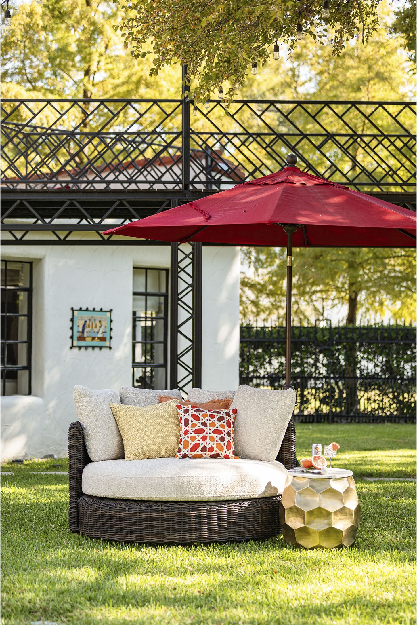 Outdoor furniture featuring a big round chair, pillows, and red umbrella in a backyard