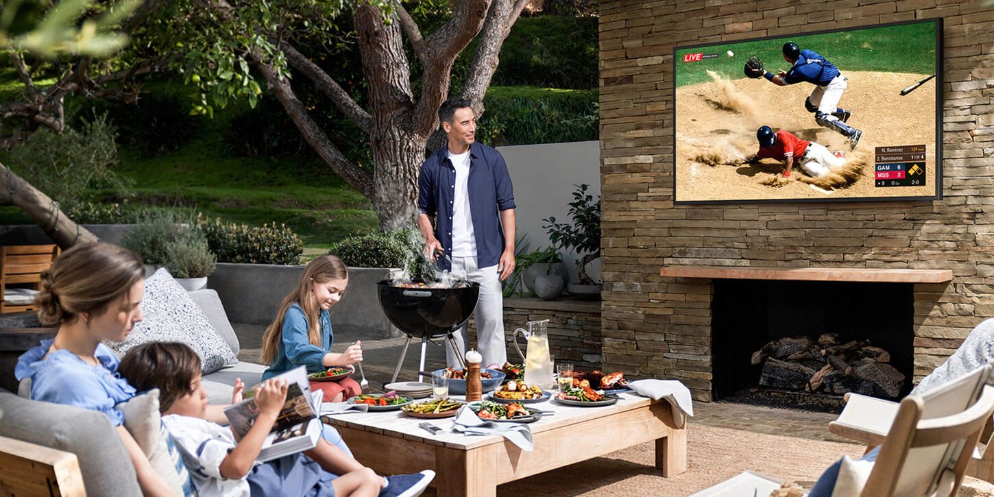 Family sitting outside in the backyard grilling and watching a football game on the tv